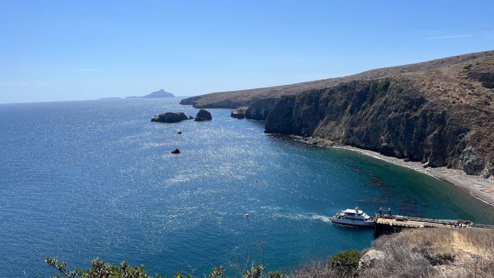 Vast coastal cliffs with a small docked boat on deep blue ocean waters, scenic California shoreline perspective.