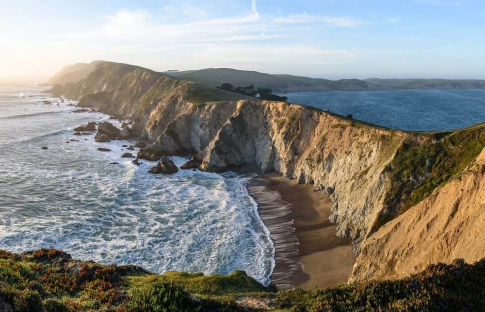 Stunning view of rugged coastal cliffs and beach at sunset, California coastline scenery, and ocean waves.