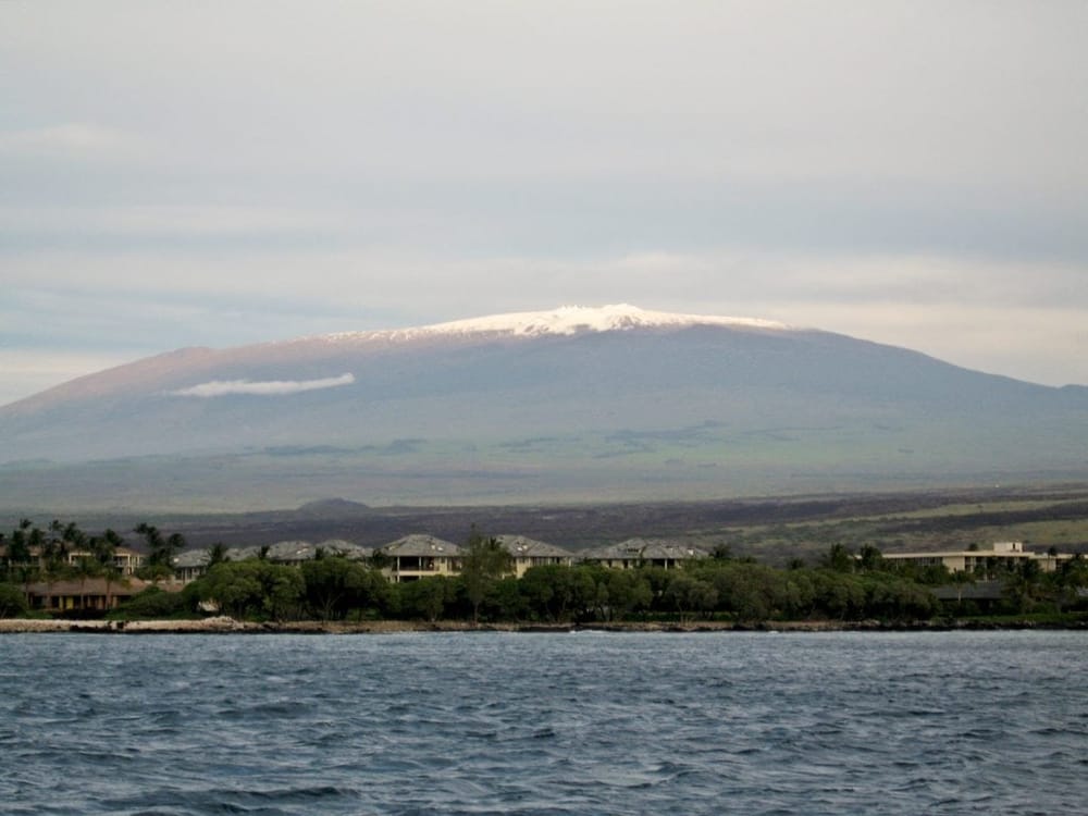 Snow-capped volcano island with oceanfront resorts and lush greenery, stunning Hawaii scenic landscape.