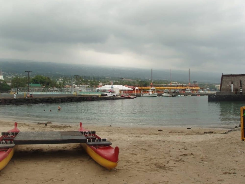 Colorful kayak on beach with harbor and boats under cloudy sky in the background.