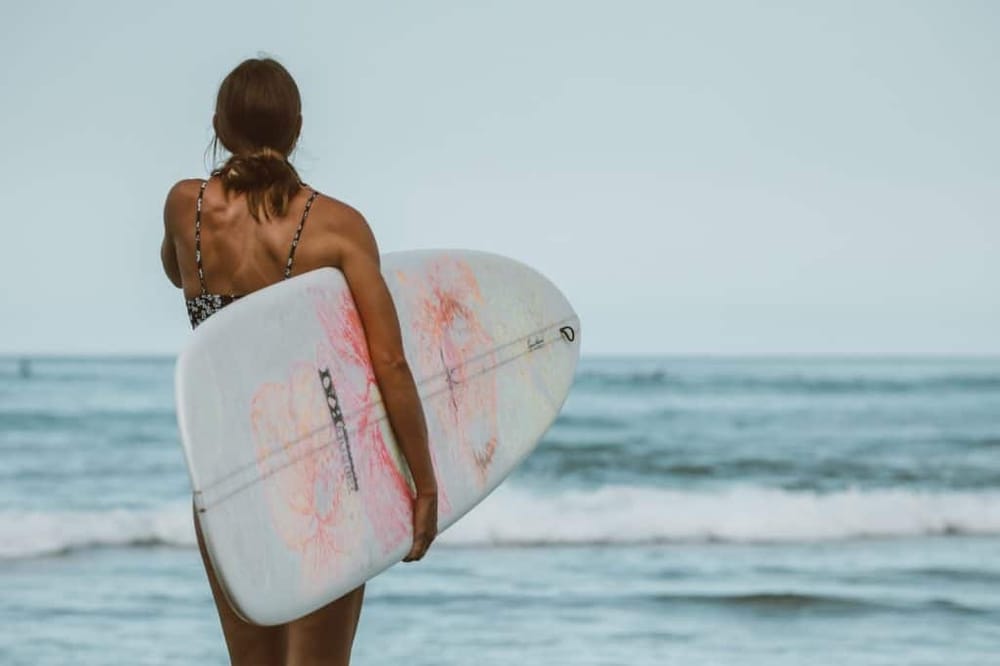 Surfer woman with a colorful surfboard at the beach, perfect for surf lessons and ocean adventures.
