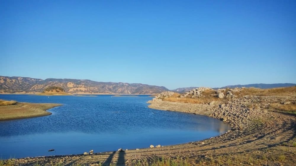 Serene lake surrounded by mountains with clear blue sky, ideal for outdoor adventures and scenic views.