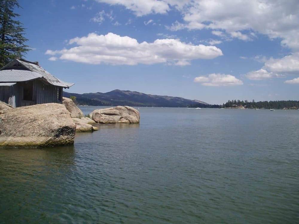 Serene lakeside view with mountains, rocks, and an old wooden boathouse, perfect for outdoor exploration and scenic photography.