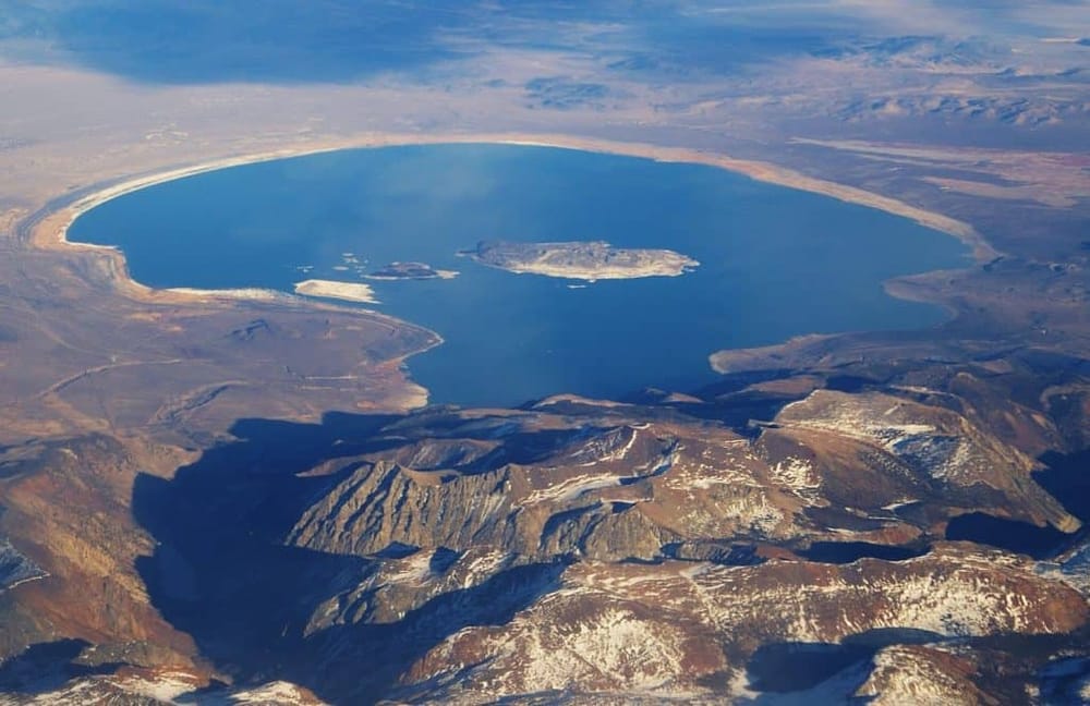 Aerial view of a large, circular lake surrounded by mountain ranges and desert terrain, highlighting natural landscape and scenery.