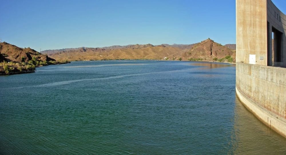 Sunset at a scenic reservoir with mountains in the background, featuring a modern dam structure on the right.