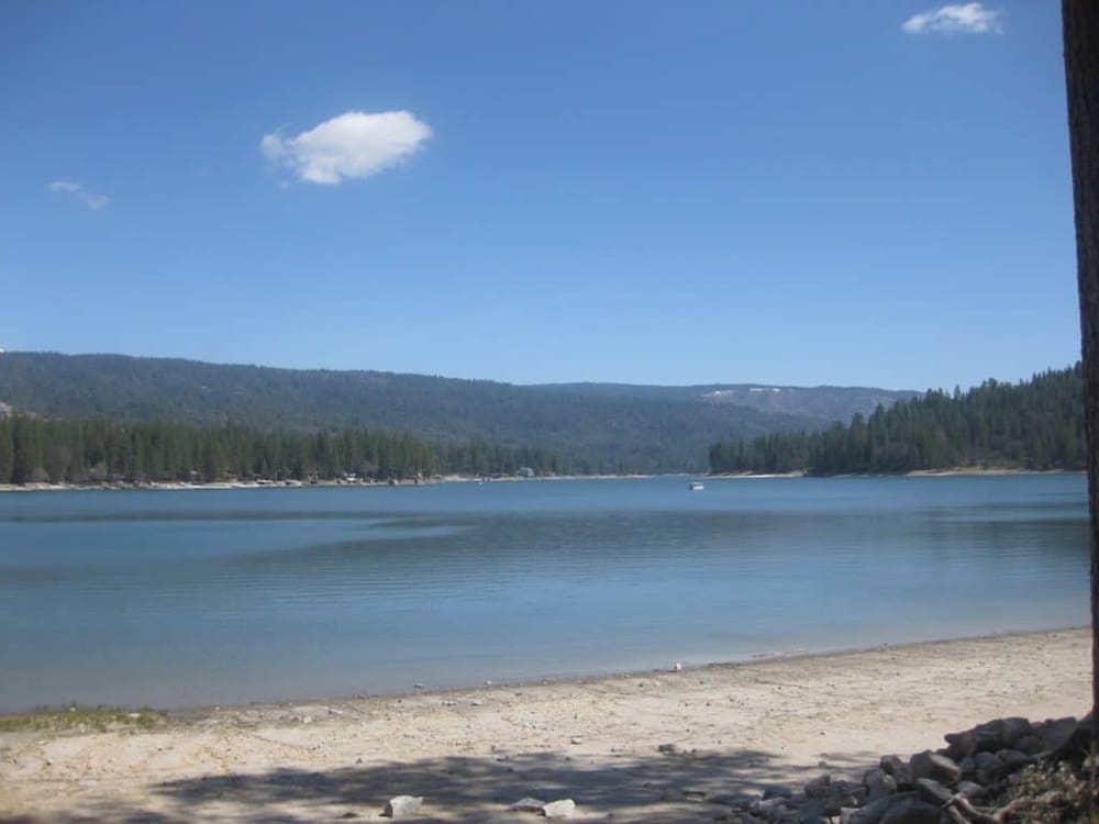 Serene lakeside view with calm water, forested mountains, and a clear blue sky, ideal for outdoor recreation.