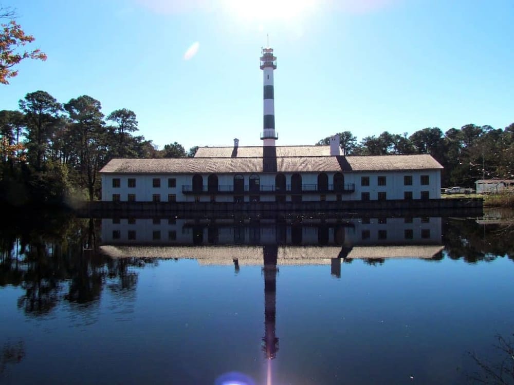 Lighthouse with historic lighthouse keeper's house reflected in calm water, scenic coastal navigation landmark.