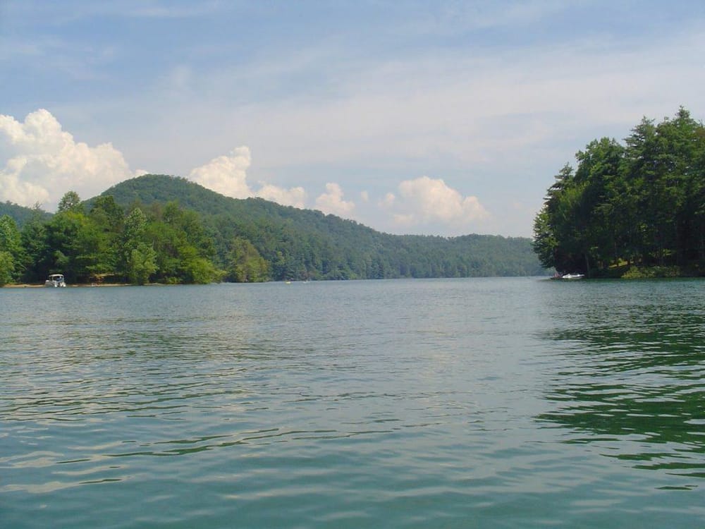 Serene lake surrounded by lush green trees and mountains under a partly cloudy sky.