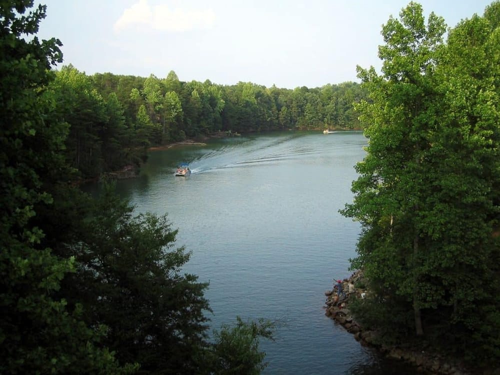 Quiet lake surrounded by lush green trees, ideal for boating and outdoor recreation.