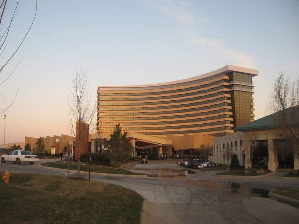 Modern hotel building with curved architecture and surrounding parking lot at sunset.
