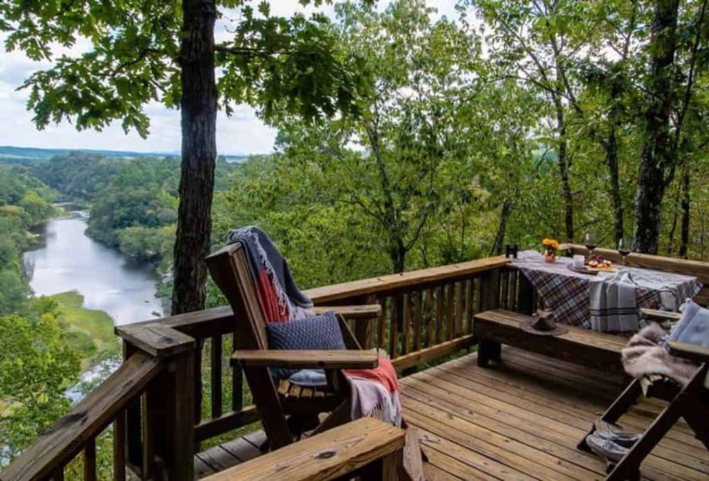 Serene outdoor deck overlooking lush forest and river landscape, perfect for relaxing and enjoying nature.