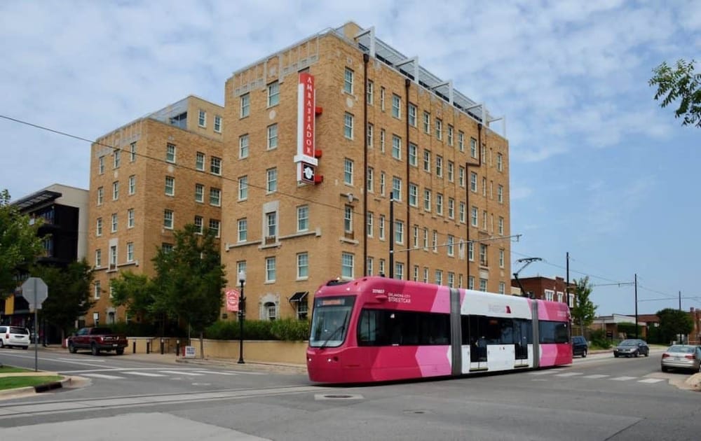 Modern pink streetcar on city street near brick apartment building in Oklahoma City.
