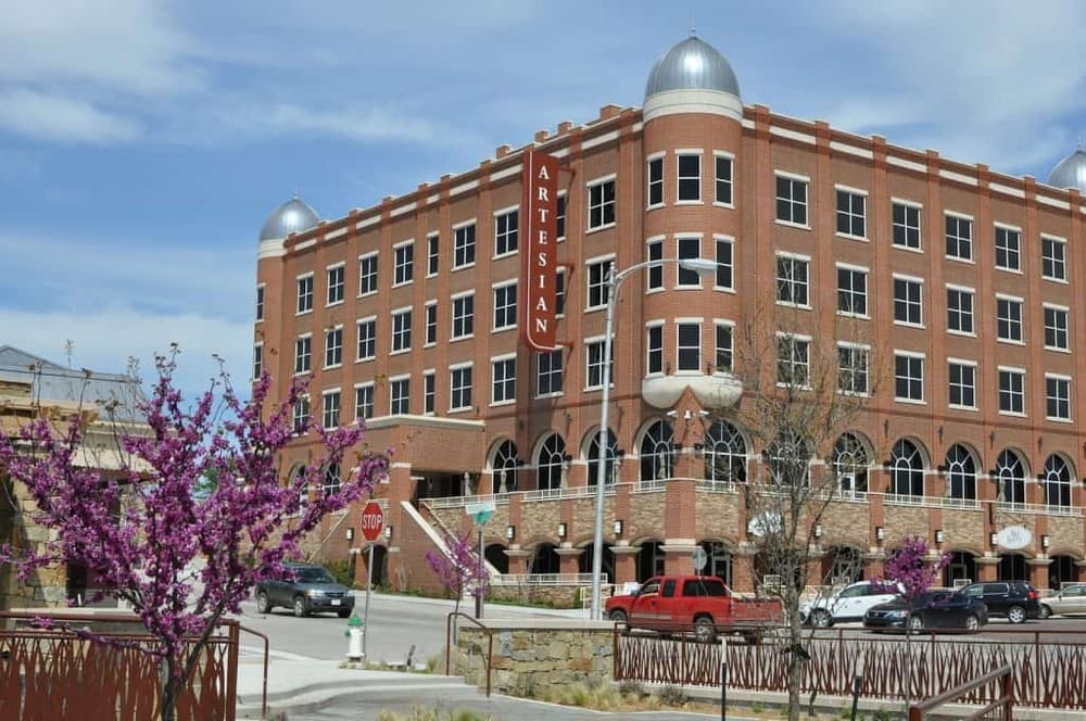 Colorful downtown building with "Artisan" sign, blooming trees, and city street view.