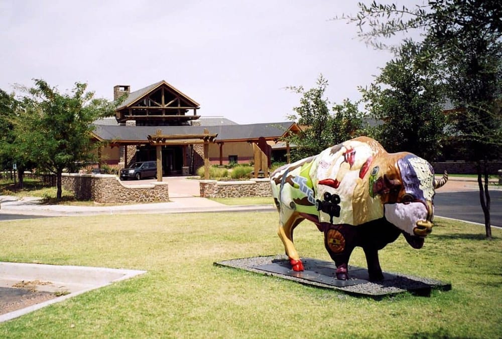 Colorful cowboy-themed cow sculpture outside a rustic building in Texas.