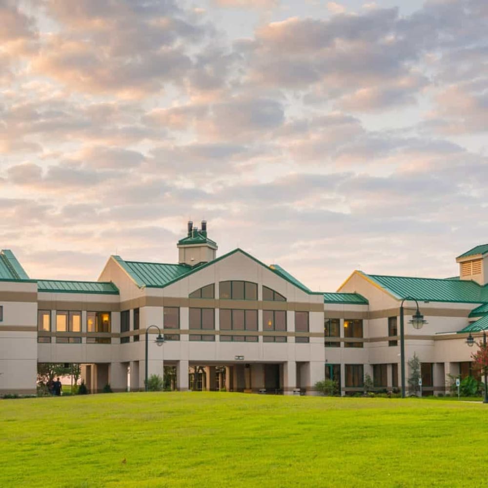 Modern hotel building with green roofs and surrounding green lawn, sunset sky in background.