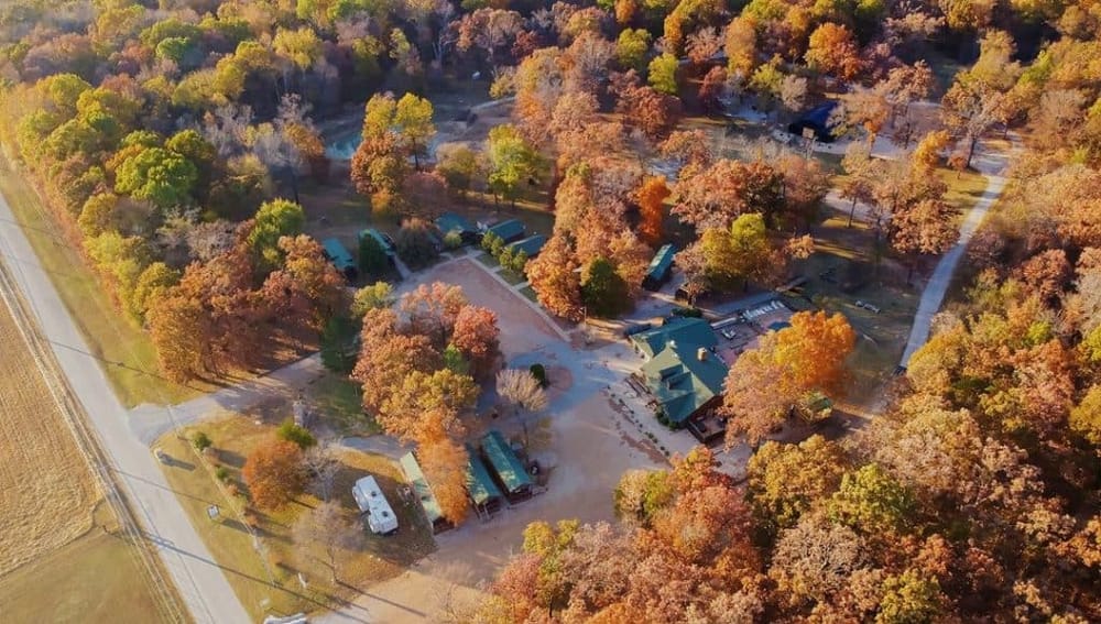 Aerial view of a wooded area with cabins and dirt pathways in fall, showcasing outdoor adventures and scenic nature experiences.