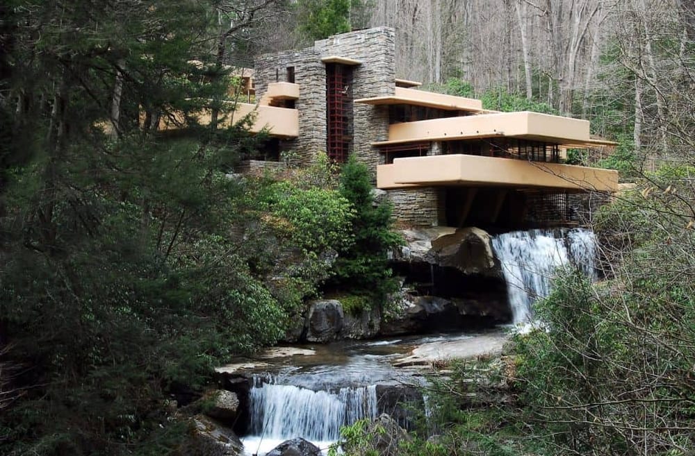 Modern house built on a rocky hillside with waterfalls and lush greenery surrounding it.
