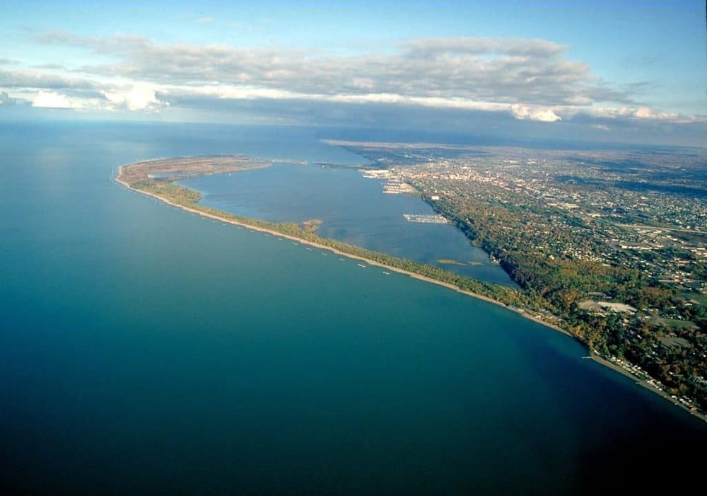 Aerial view of a coastal city and river with lush greenery and urban areas in sunny weather.