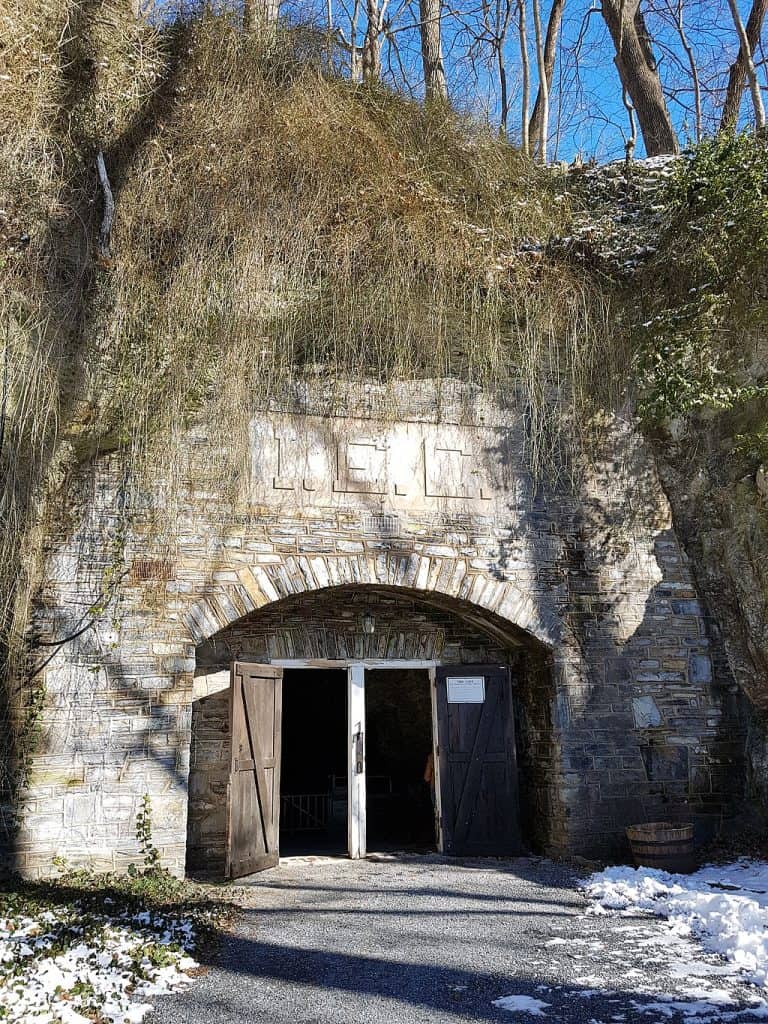 Old stone tunnel entrance surrounded by trees and snow, historical site, scenic nature trail access.