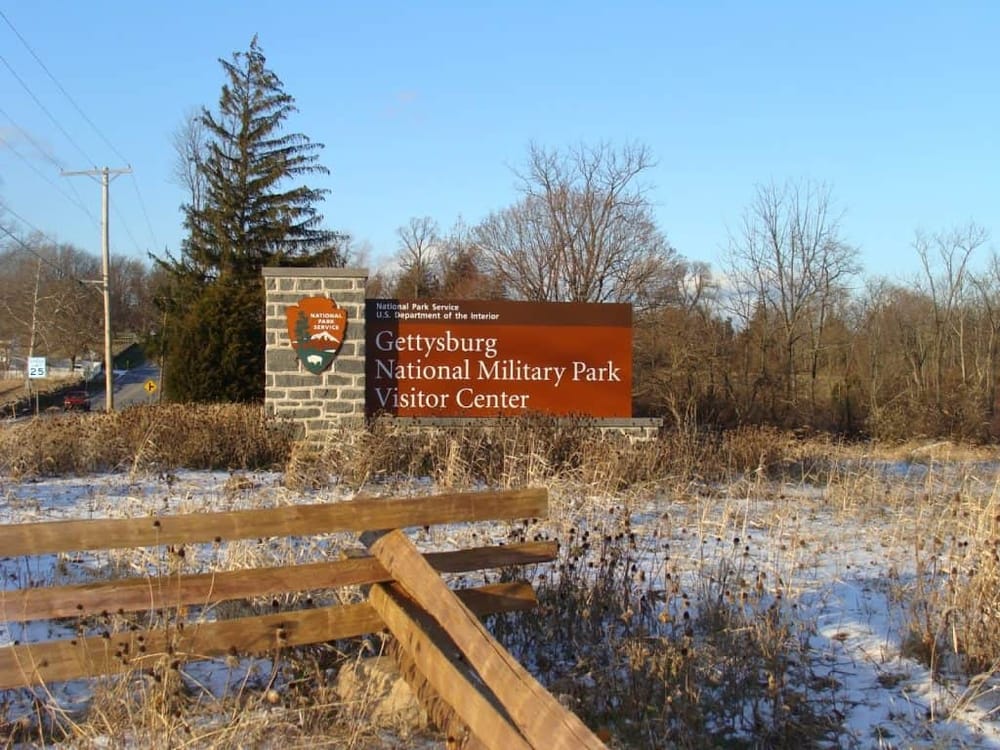 Gettysburg National Military Park visitor center sign in outdoor winter setting, surrounded by trees and snow.