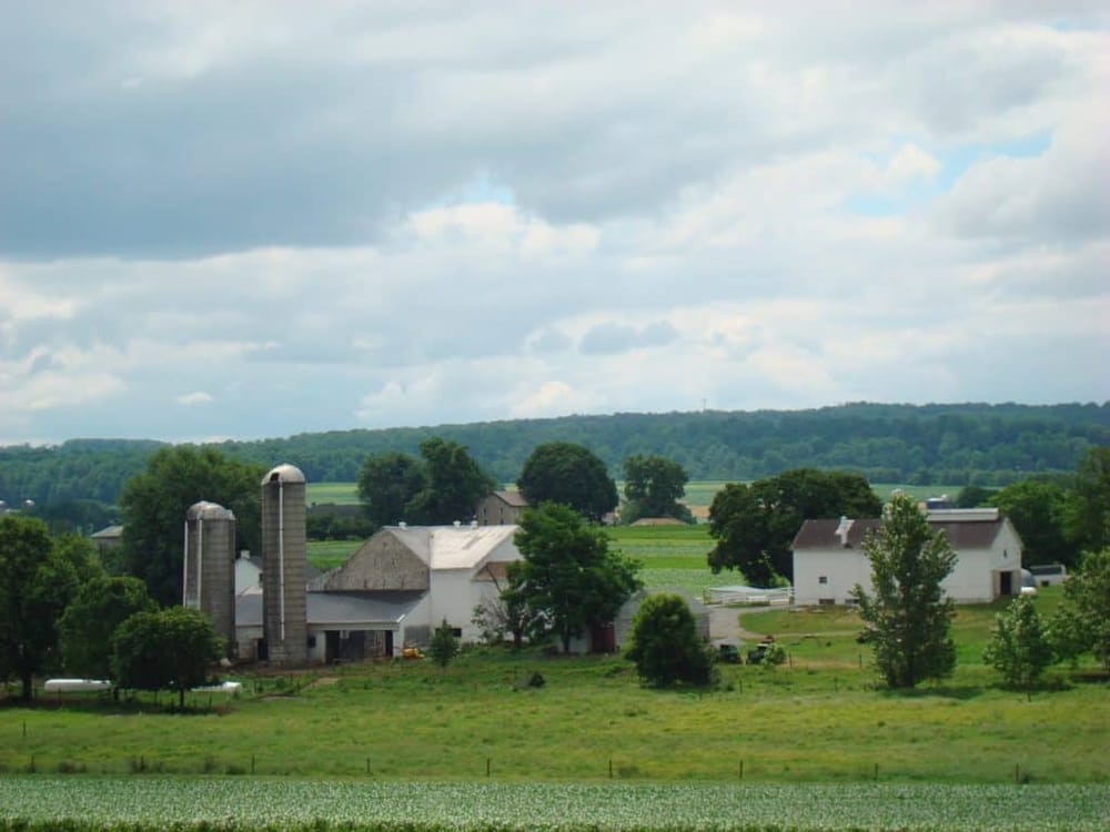 Rustic farm landscape with barns, silos, and rolling green hills under cloudy sky, ideal for rural travel and farmstead exploration.