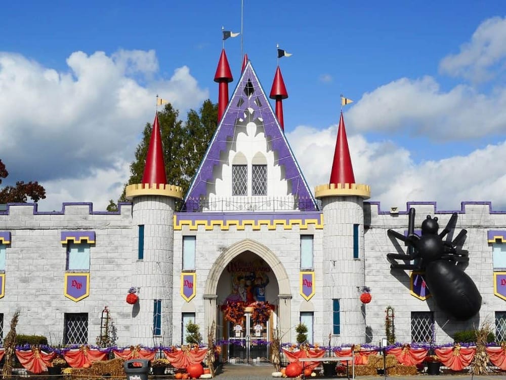 Colorful Disney-themed castle with Halloween decorations, pumpkins, and a giant spider sculpture, perfect for family fun.