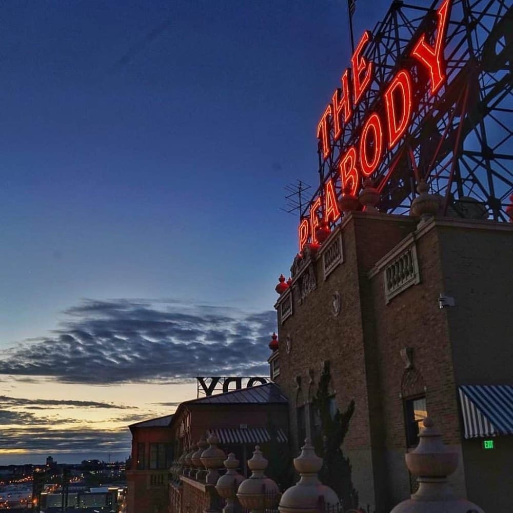 Lively neon sign above historic brick building at dusk, vibrant cityscape below.
