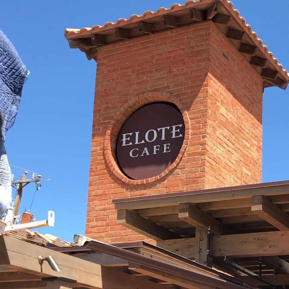 Bright red brick clock tower building with "Elote Cafe" sign, sunny weather, and clear blue sky.