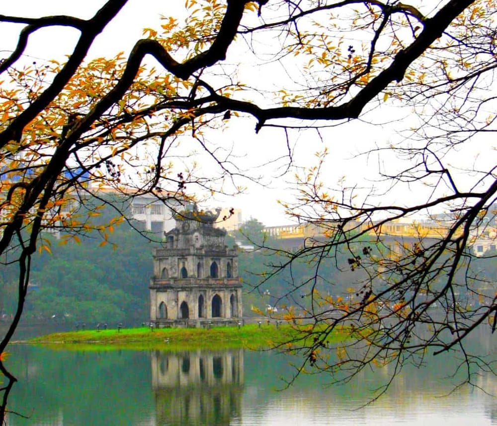 Ancient pagoda reflected in lake with tree branches, Hanoi Vietnam, scenic travel destination.