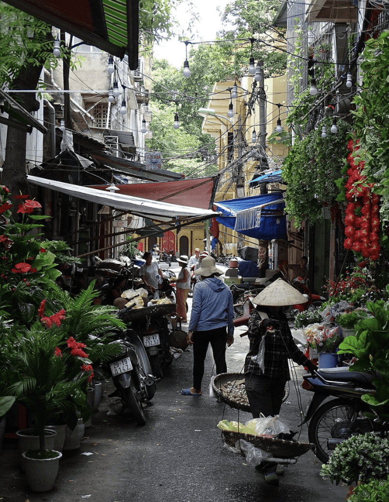 Colorful street market with local vendors, vibrant flowers, and bustling atmosphere in Hanoi, Vietnam.