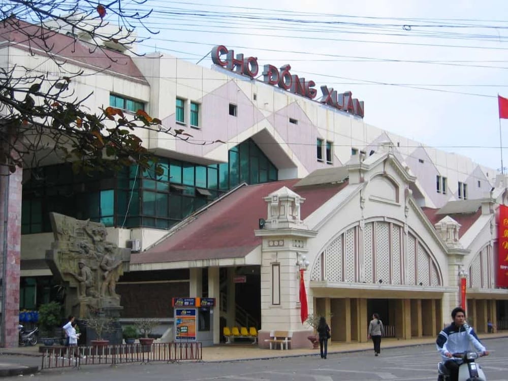 Modern architecture of Cho Dông Xuan building in Hanoi, Vietnam, with street scene and pedestrians.