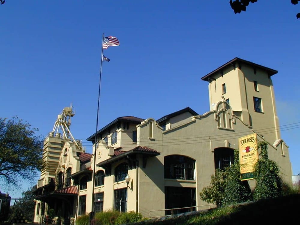 Historic distillery building with American flag flying, featuring Spanish-style architecture, in a sunny setting.
