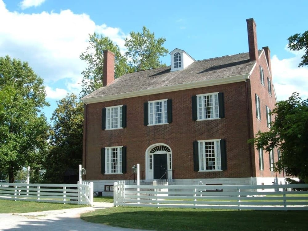 Historic brick house in Georgia, surrounded by lush trees and a white picket fence.