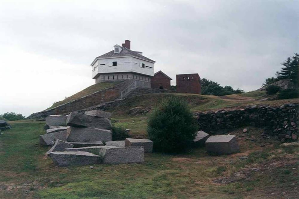 Historic lighthouse on a grassy hill with scattered rocks and cloudy sky, part of QuestForDirections navigation guides.