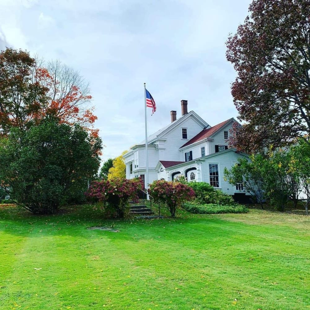 Historic white American house with landscaped garden and American flag, autumn foliage, peaceful setting.