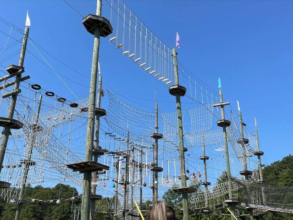High ropes adventure course at Quest For Directions, outdoor team-building activity, zip lines, obstacle course, wooden structures, safety gear, kids and adults.