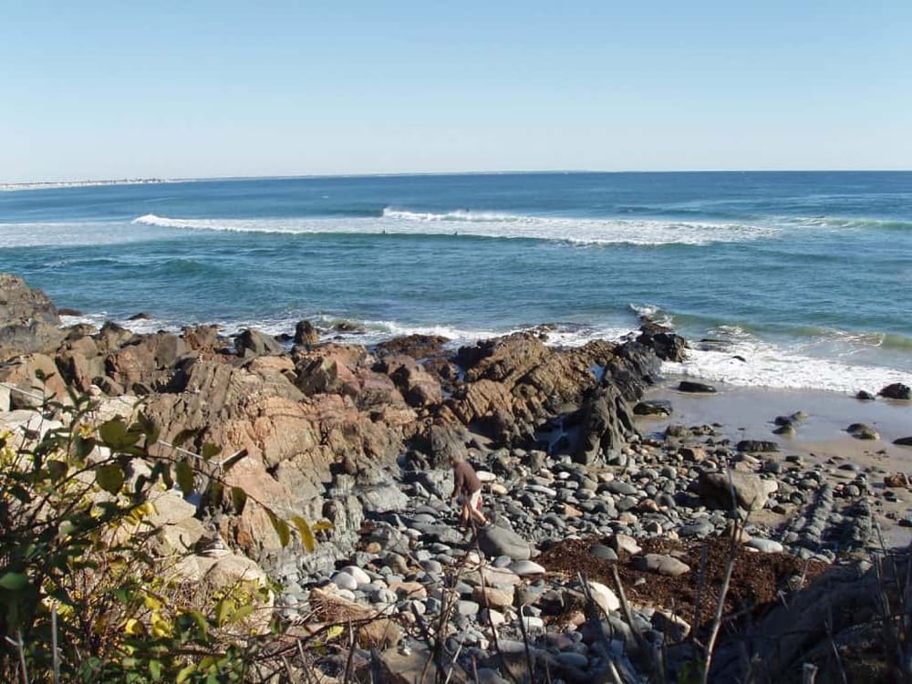 Coastal rocks and sandy beach with ocean waves, scenic shoreline, and clear blue sky at QuestForDirections.