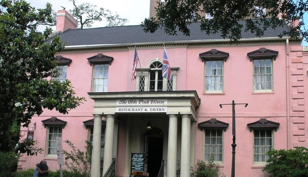 Colorful pink historic restaurant building with flag displays and colonial architecture, offering a charming dining experience.