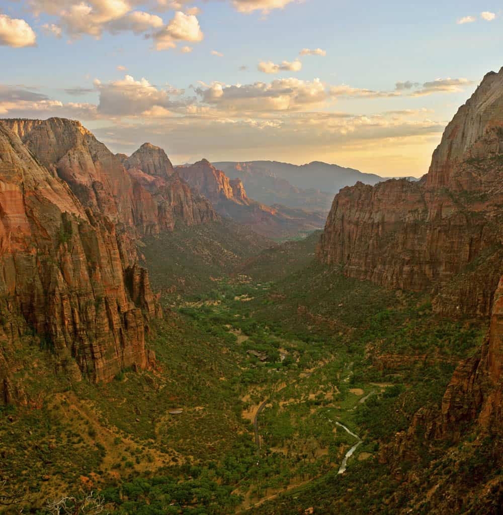 Vast canyon landscape with colorful rock formations and lush green valley at sunset.