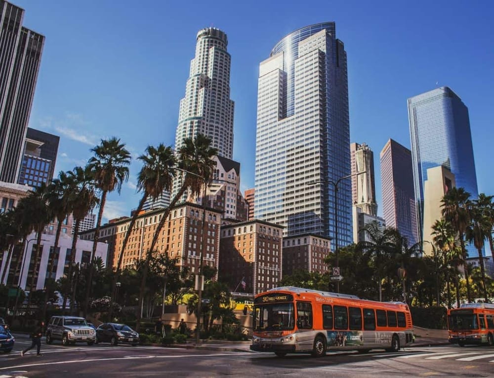 Vibrant Los Angeles cityscape with skyscrapers, palm trees, and Orange Metro bus on downtown streets.
