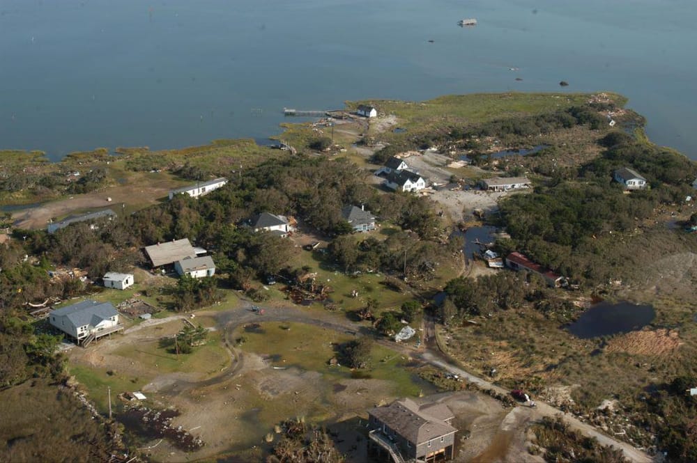 Aerial view of a coastal neighborhood with houses, greenery, and water, showcasing scenic oceanfront living.