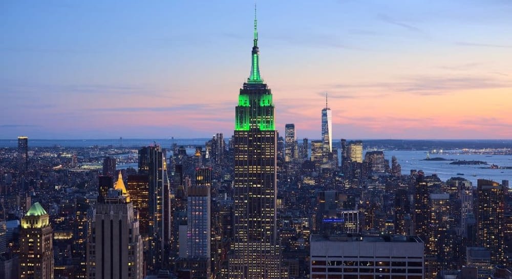 Panoramic view of Empire State Building illuminated in green, New York City skyline at dusk.