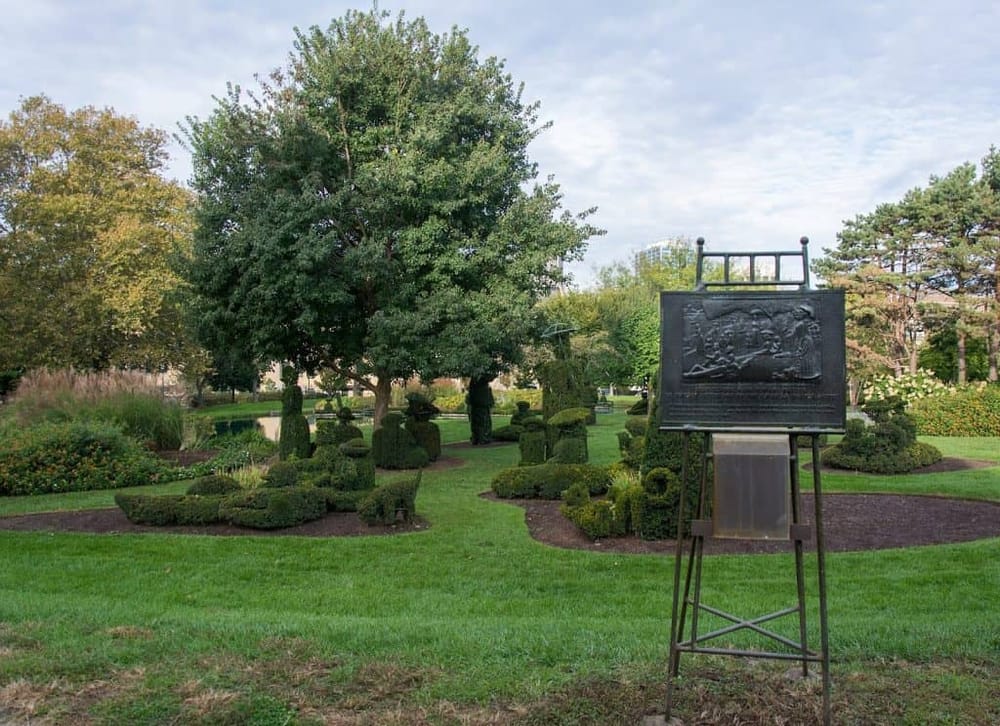 Lush park with manicured topiary and a bronze memorial plaque, perfect for outdoor exploration.
