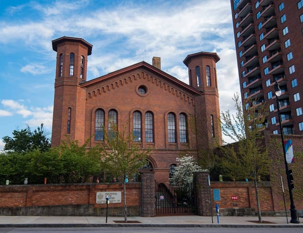 Historic brick church in city with modern high-rise building nearby, showcasing urban architecture and cultural landmarks.