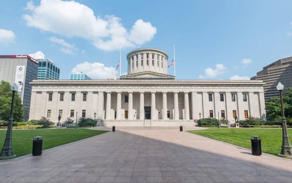 Grand historic courthouse with white columns and American flags, modern city skyline in background.