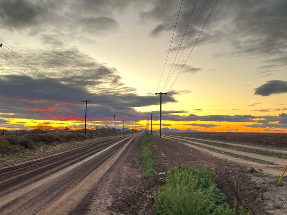 Wilderness dirt road with sunset sky, power lines, and open plains, ideal for QuestForDirections navigation.