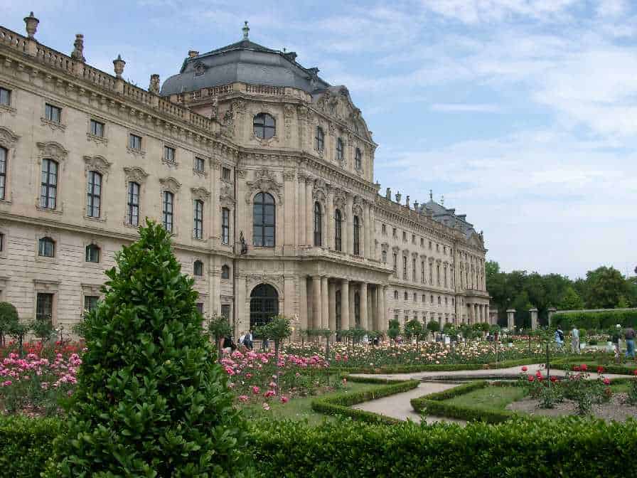 Elegant historic palace with lush gardens and blooming flowers in a scenic cityscape.