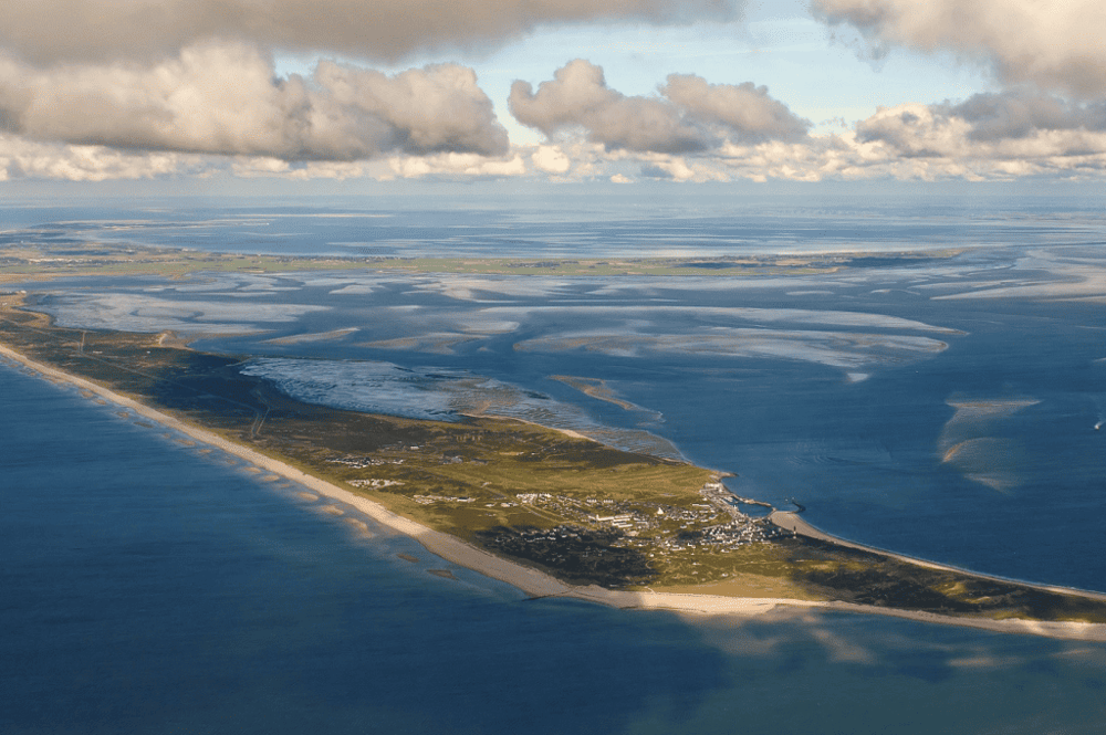 Aerial view of a coastal area with salt ponds, wetlands, and a small community under a cloudy sky.