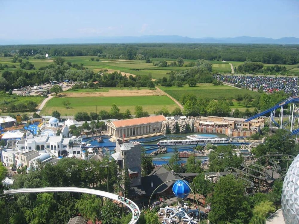 Colorful amusement park with roller coasters, water rides, and green countryside in the background.