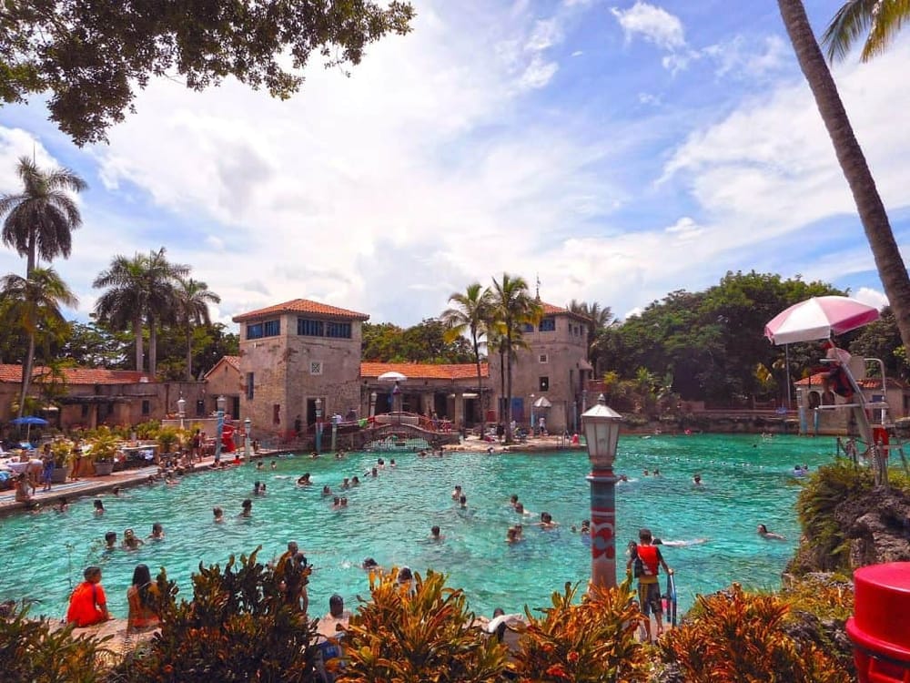 Outdoor swimming pool at a tropical resort with palm trees and historic buildings, perfect for vacation relaxation and water activities.
